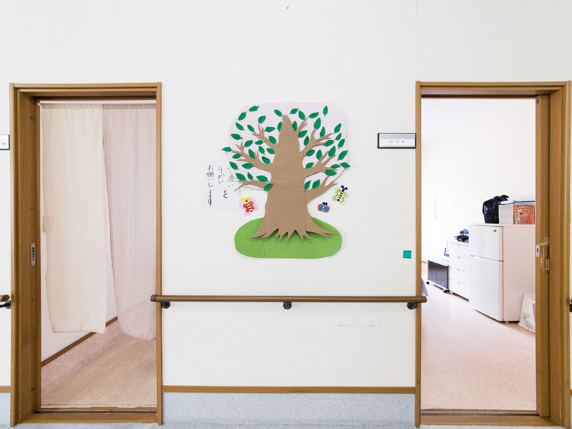 レースの暖簾が掛かっている居室横の壁には、手すりが取り付けられ色画用紙を切って作られた木や蝶が飾られている。