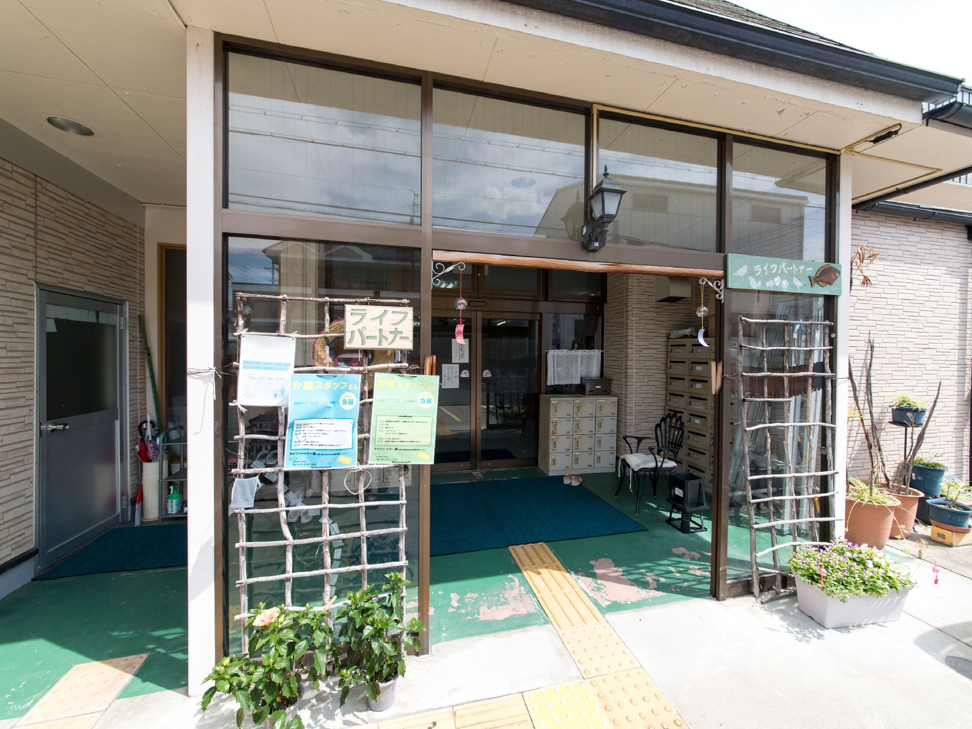 玄関の両脇には、プランターが置かれている。中にはロッカーや椅子が配置されており、壁側には郵便受けが設置されている。