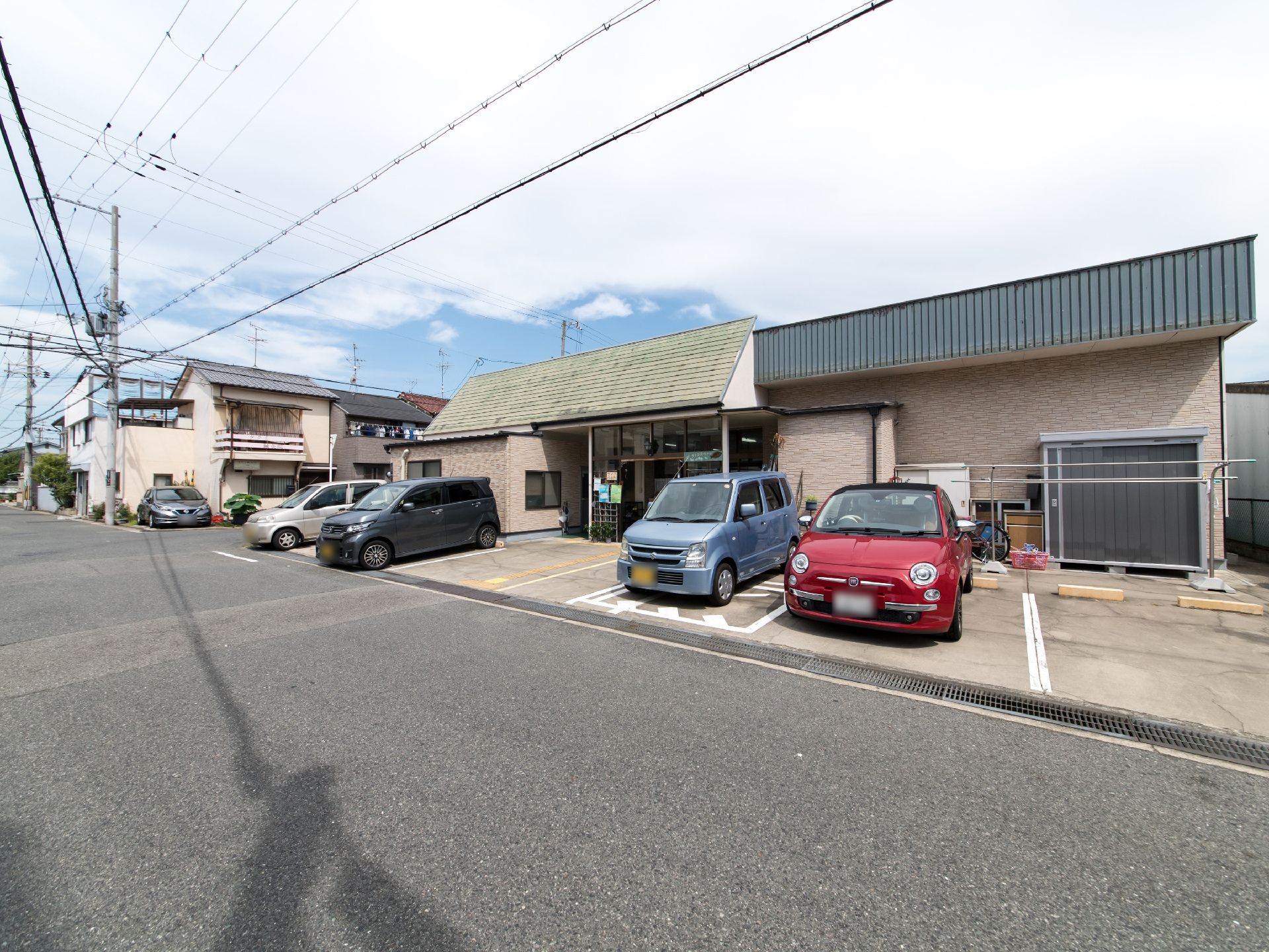 駐車スペースを正面に設けている施設である。誘導ブロックが玄関先に設置されており、建物の壁際に物置と物干し台が置かれている。