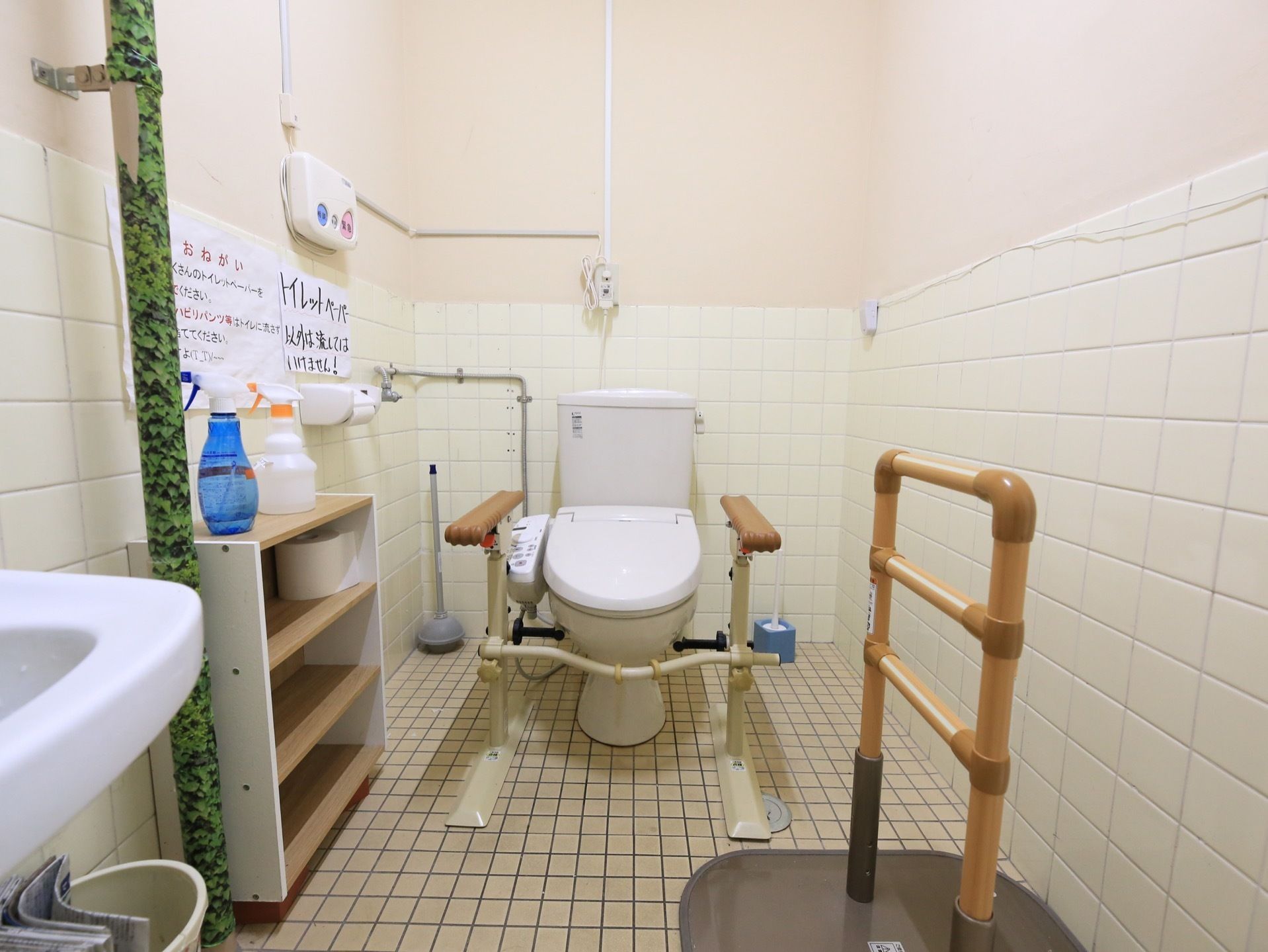洗面台を備えた奥行きのあるトイレがある。温水洗浄機能付きで、便座の両側には手すりが備えられている。