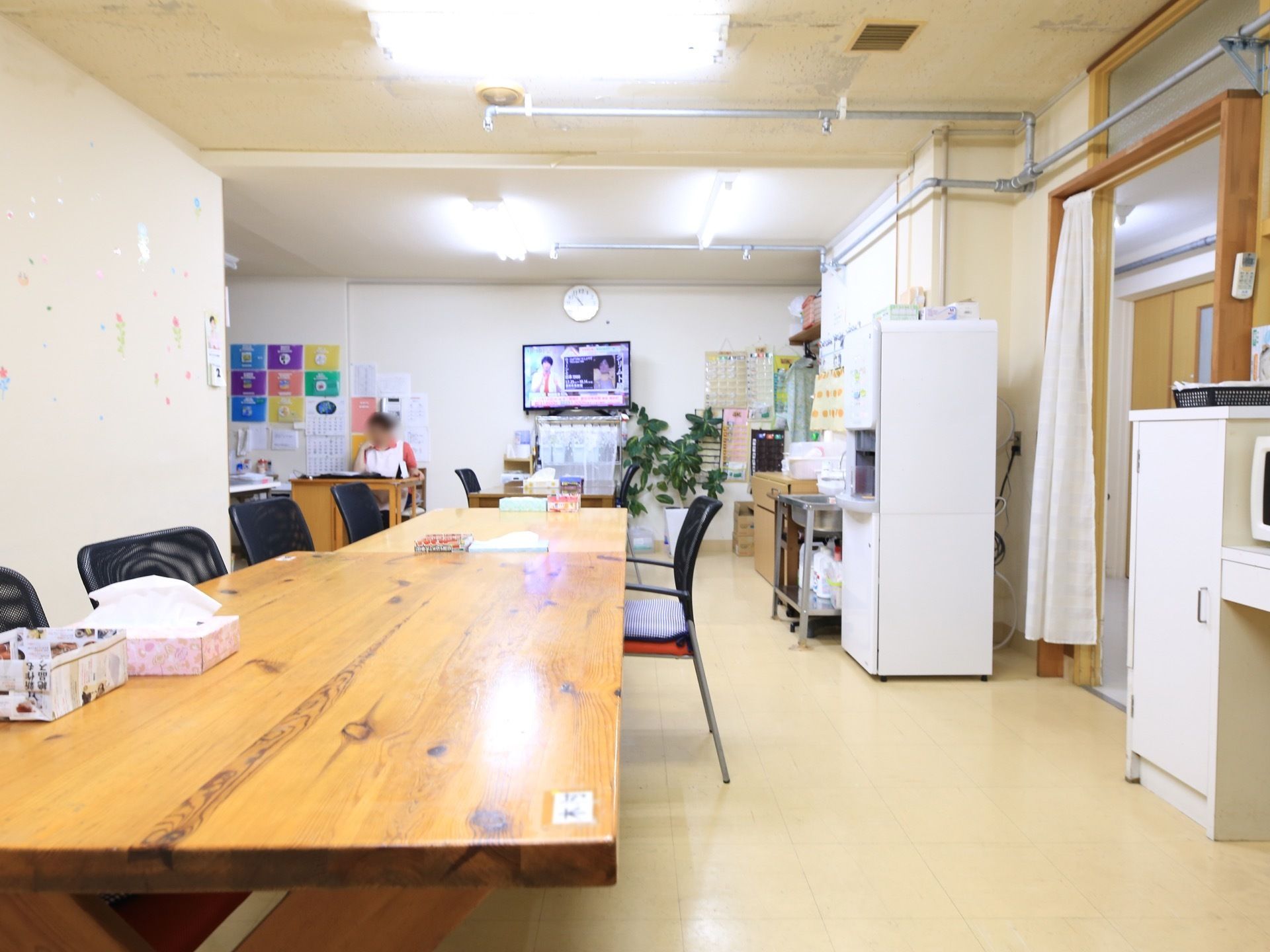 木製のテーブルが並べられた小部屋があり、給水器や電子レンジが置かれている。スタッフが１人、机に向かっている。