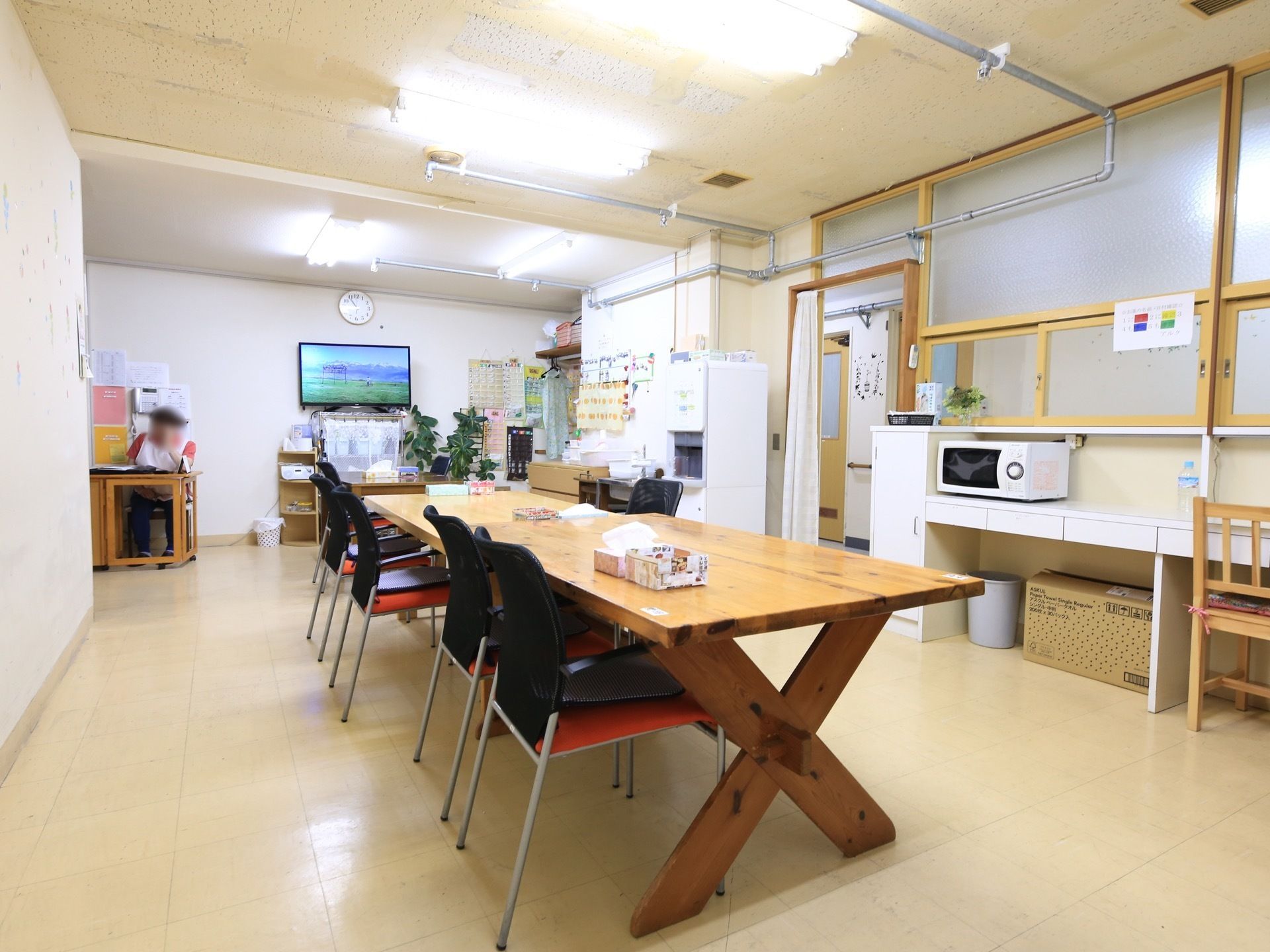テーブルセットが置かれた部屋があり、奥で女性のスタッフが作業をしている。壁にはテレビがある。