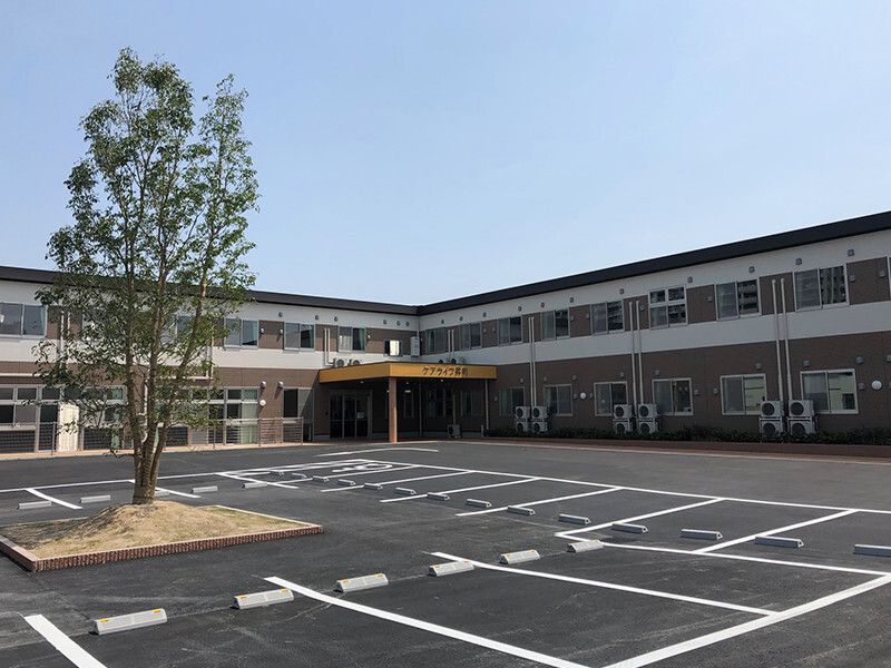 広い駐車場が付いた２階建ての建物はエル字型で玄関には大きな屋根が付いている。