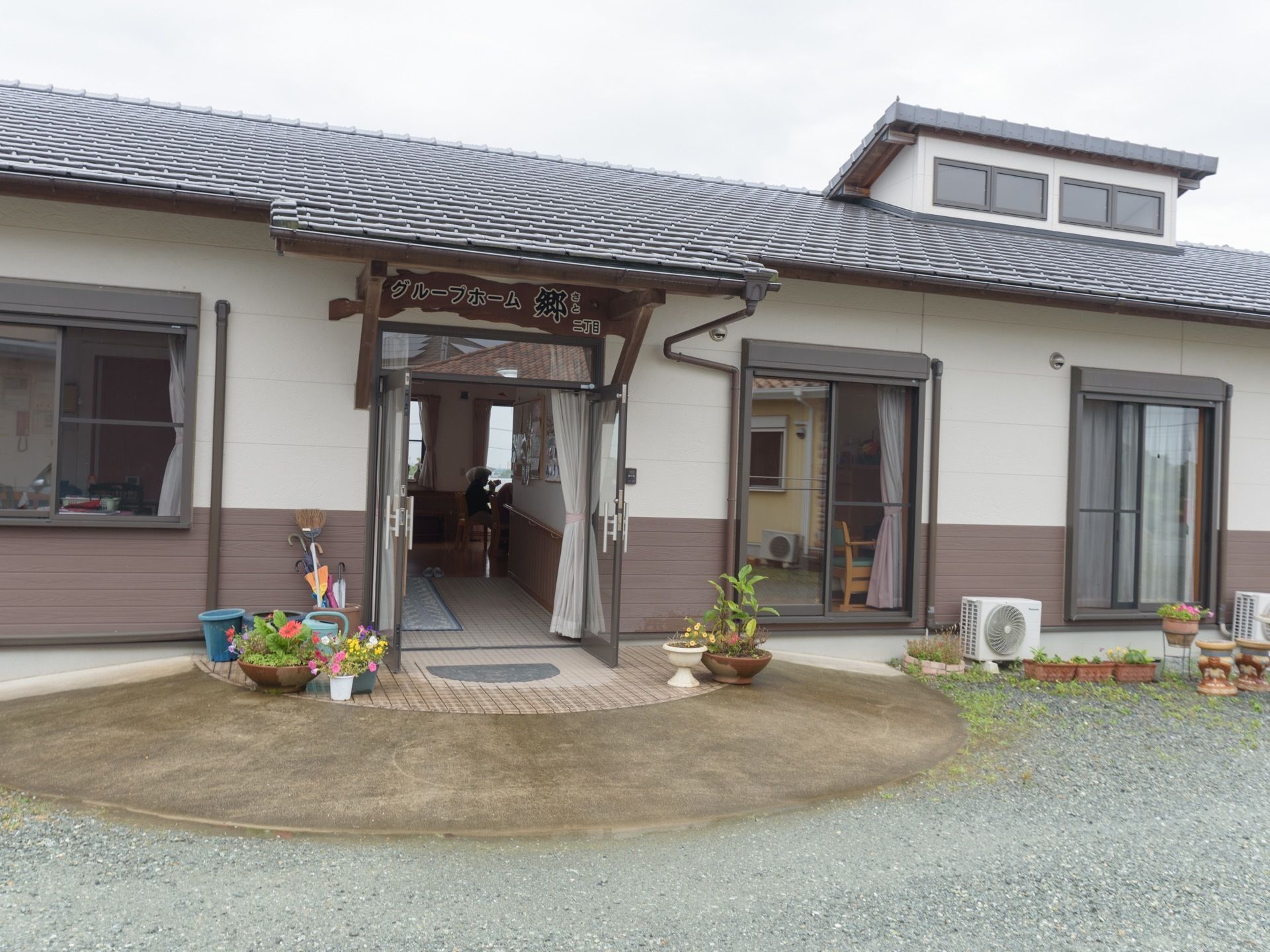 建物の入口ドアは、両開きのガラス製。周りには花などが植えられたたくさんの植木鉢が置いてある。玄関上部には施設名の看板が取り付けられている。