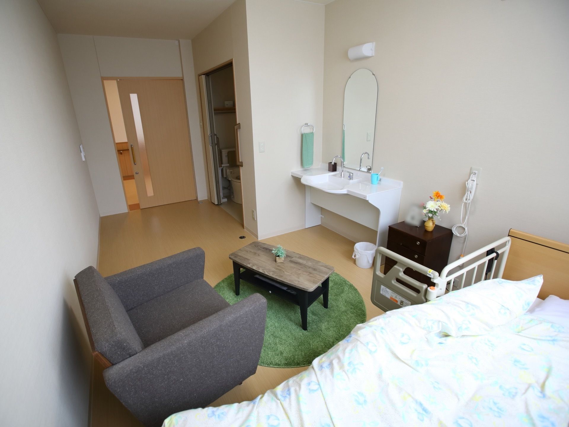 ワンルームの居室で、白色と木目調のデザインとなっている。トイレのほか、洗面台も完備。マットやテーブル、ソファーが置いてある。