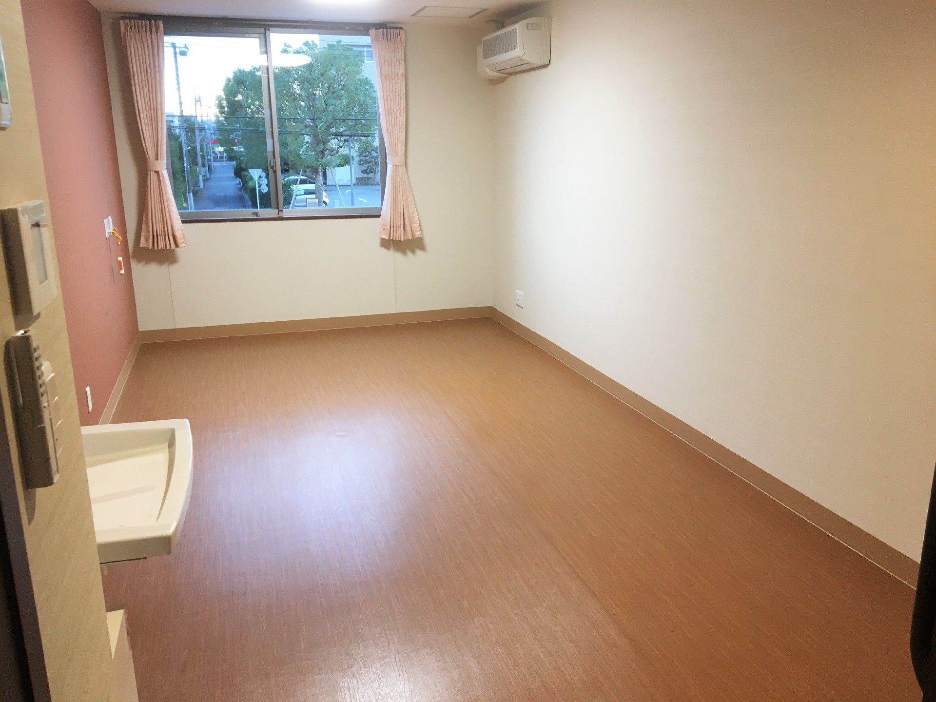 窓の向こう型に景色が見えている施設内の居室の様子。手前に洗面台がついている空間