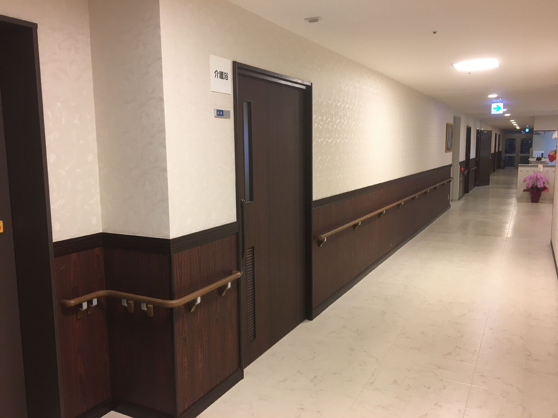 濃い色合いのドアがついた施設の居室入り口。廊下にはまんべんなく手すりが取り付けてある様子