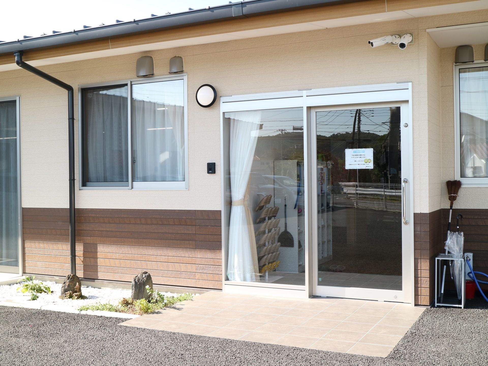 施設入口のドアはスライド式でガラス張りになっている。その周囲には、防犯カメラやインターホン、ポーチライトが設置されている。