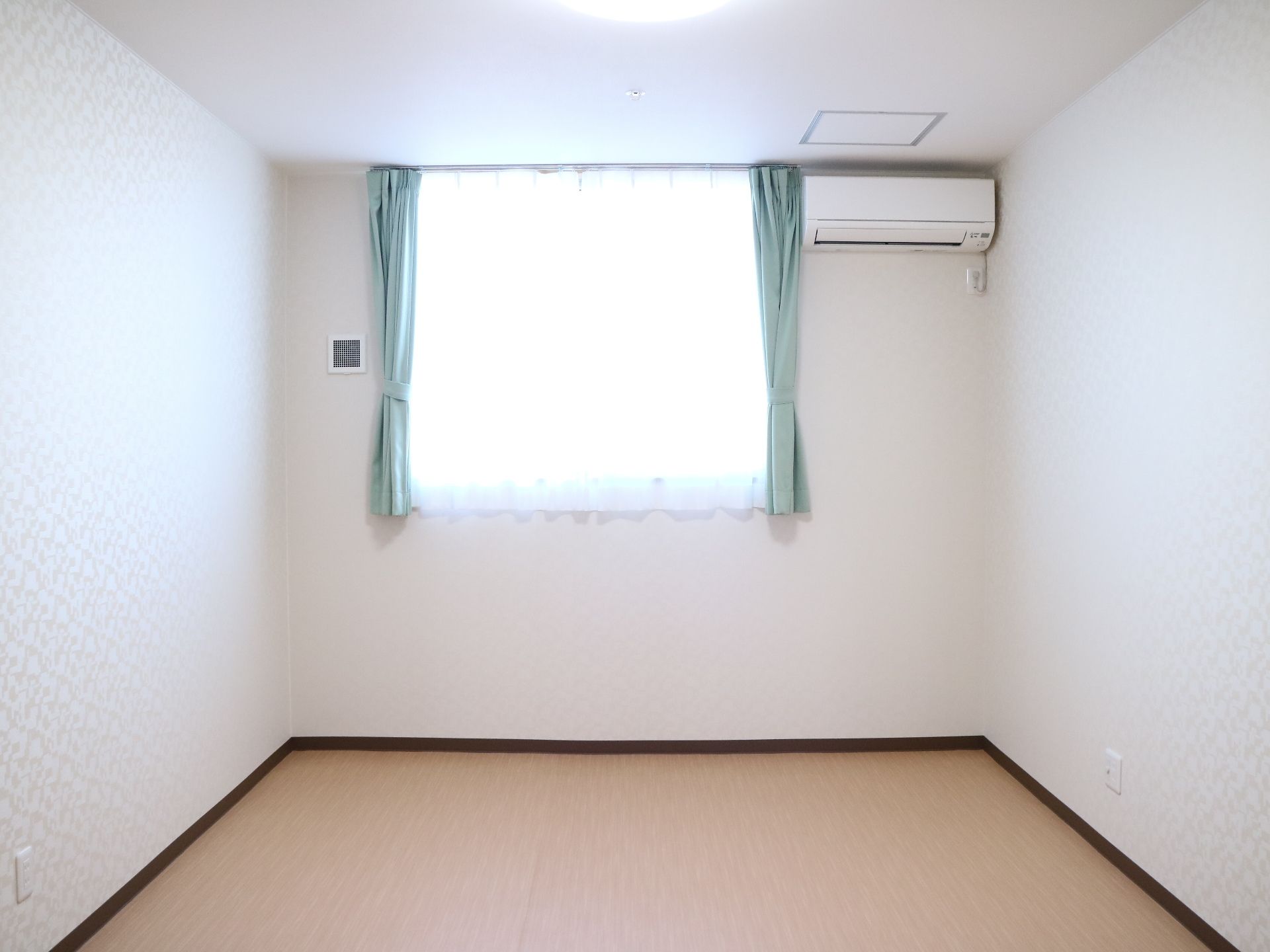 デザインクロスが貼られた壁にエアコンや窓が設置されたご入居前の居室