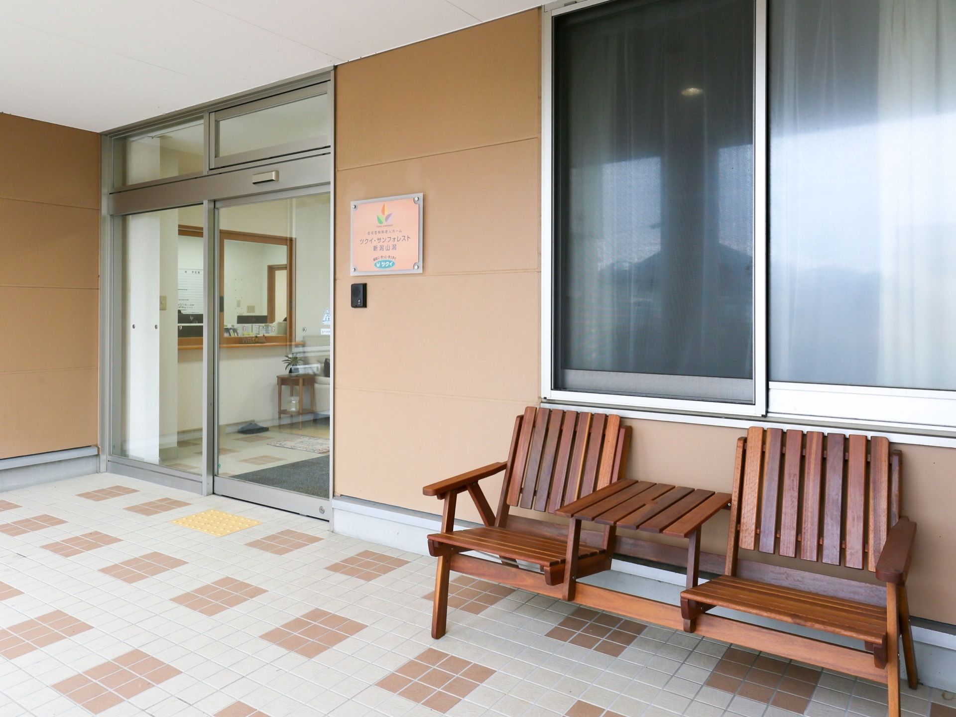 自動扉の入り口に受付があり、来訪者様の対応や入居者様の外出の見守りを行う。外にベンチを置き、座って景色を眺めたり休憩などができる。