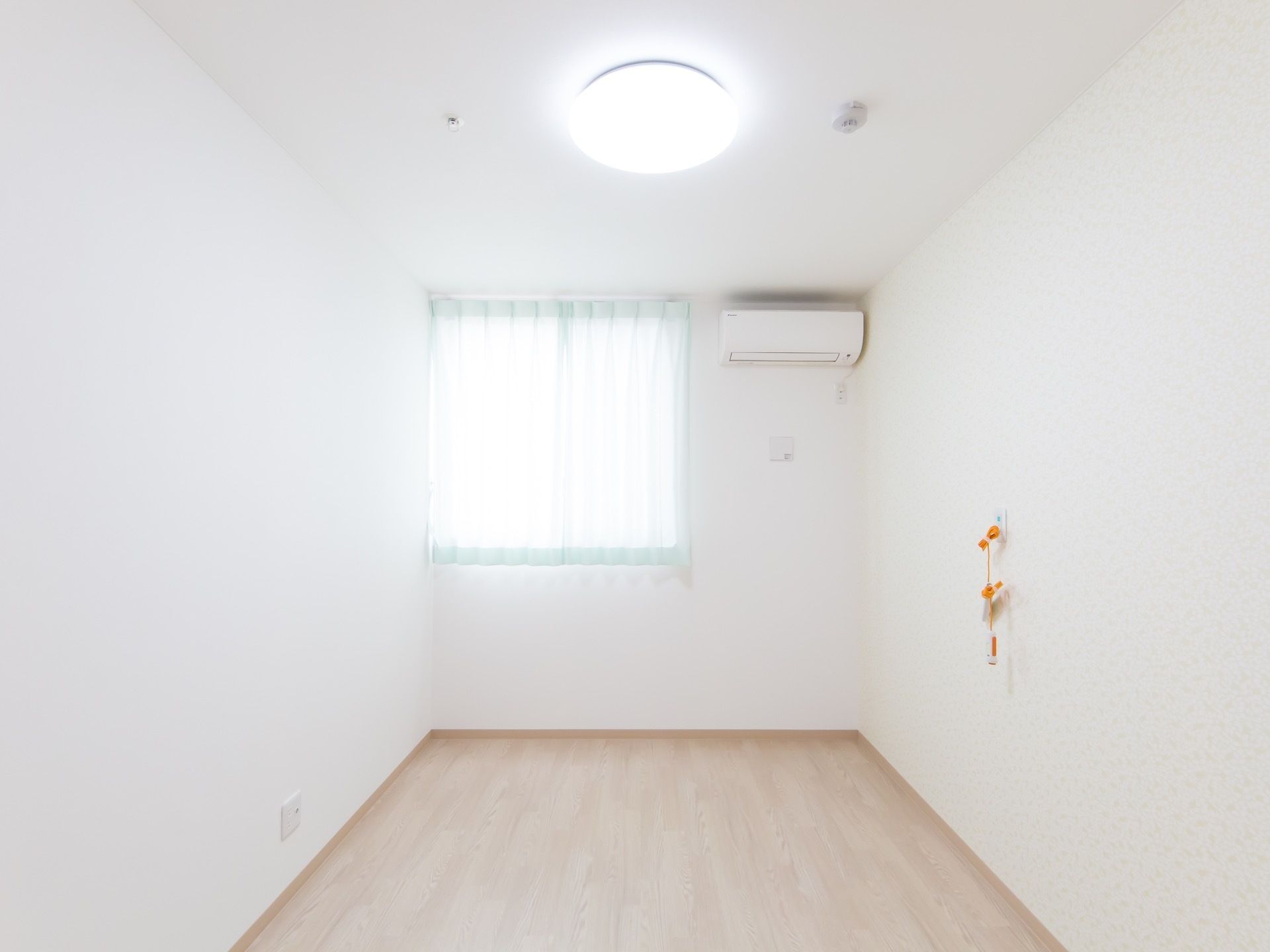 フローリングの居室である。呼び出しボタンとエアコンが設置されている。窓が大きいため、居室全体が明るくなっている。