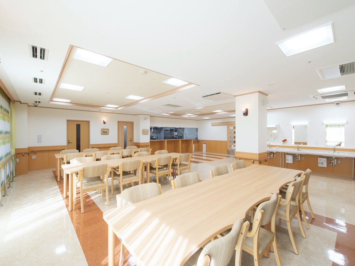 木製の大きなダイニングテーブルセットが複数置かれた明るい雰囲気の食堂のすぐそばに厨房がある。