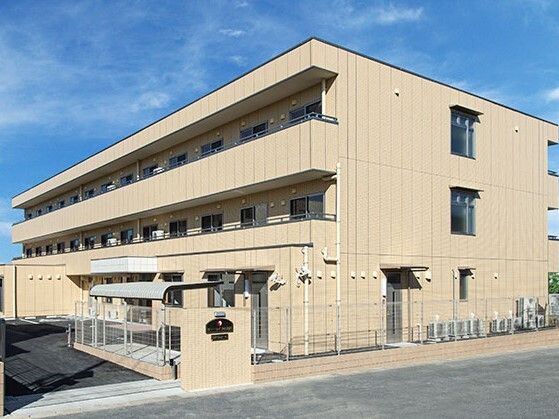3階建ての建物はベージュ系の外壁で敷地内には駐車場があり、日当たりのいい場所に建っている。