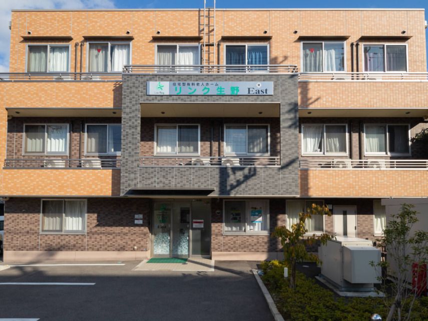 日当たりのいい場所に建っているブラウン系の外壁の3階建ての建物の前には駐車場がある。