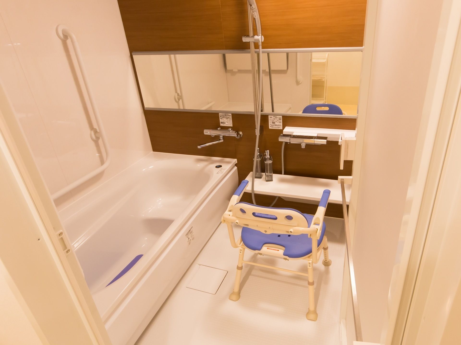 広々とした浴室で、大きい鏡や手すり、椅子がある。椅子に座りながら気持ちよく入浴することができる。