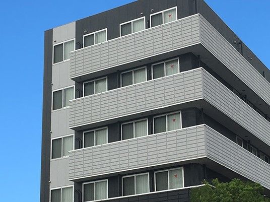 グレーと黒の６階建ての建物にはベランダが付き、緑もある。