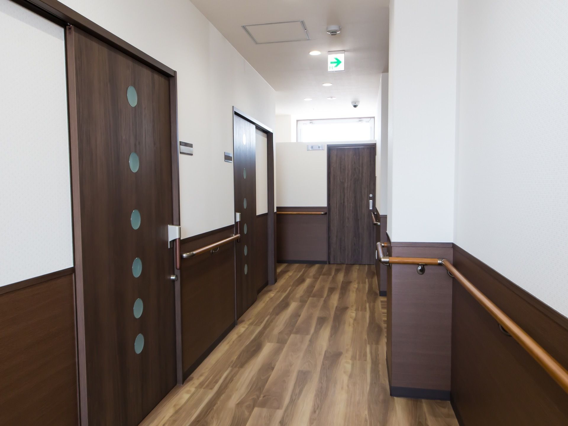 フローリングの床とダークブラウンの部屋の扉がマッチングして趣のある通路となっている。横幅も広く、壁の腰高位置には手すりがある。