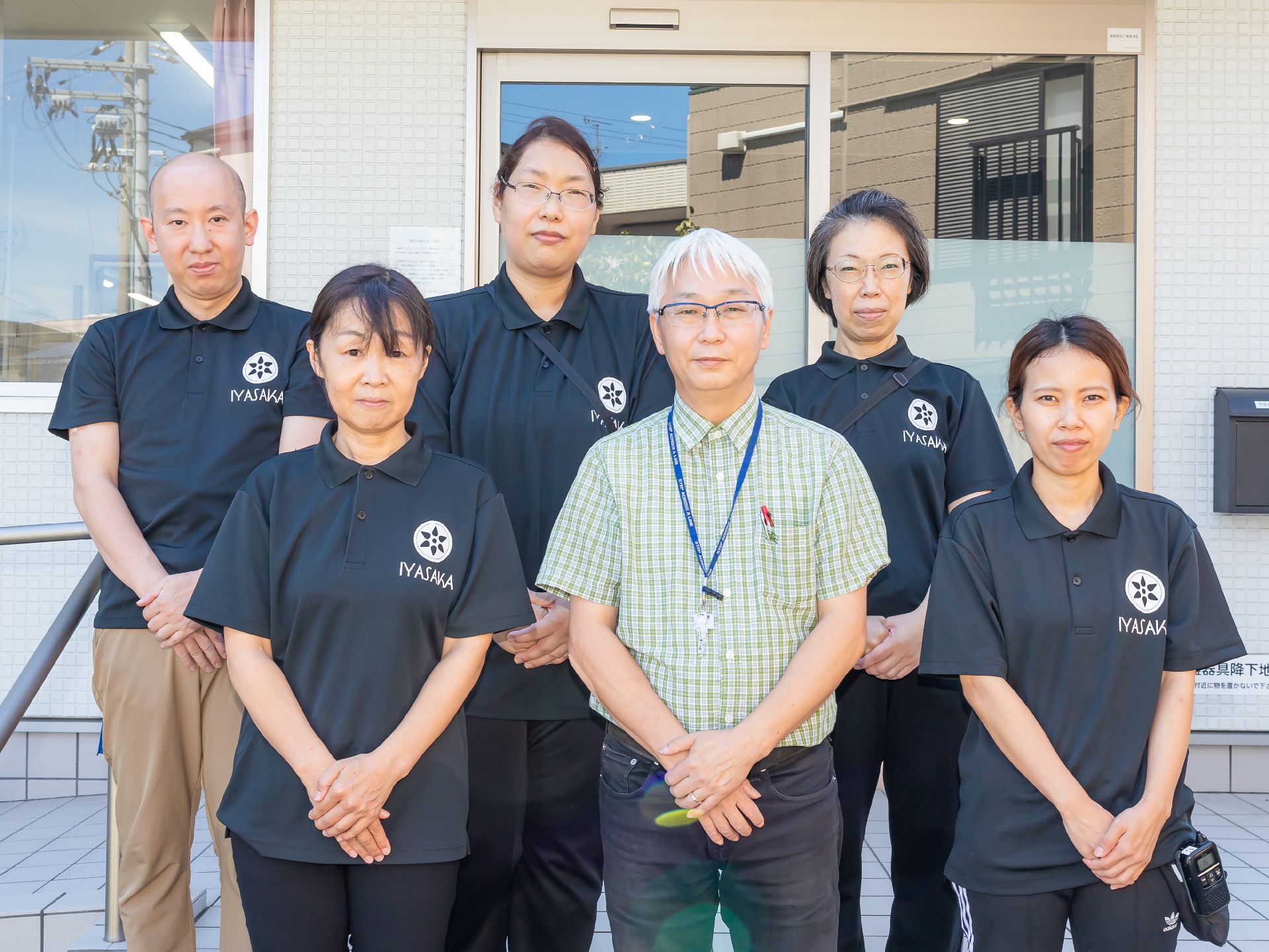 高齢者2名とスタッフが手を握りながら談笑している様子。施設内の会話の一画面