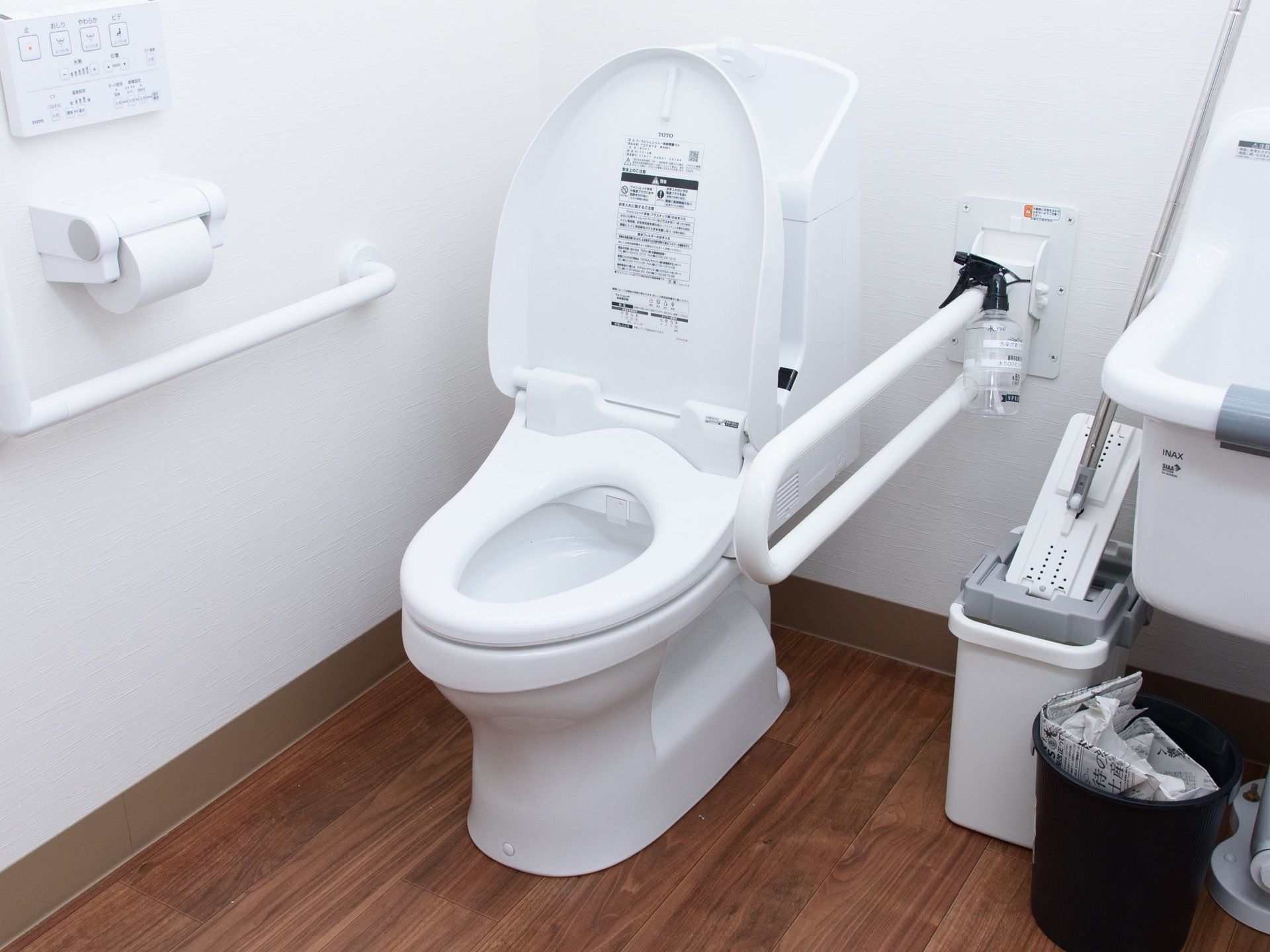 トイレの上部に手洗い場が設けられている。壁には手すりや操作パネル、ペーパーホルダーが設置されている。
