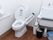 白を基調とした清潔感のあるトイレで、横には掃除用具が用意されている。温水洗浄機能付き便座が採用されている。