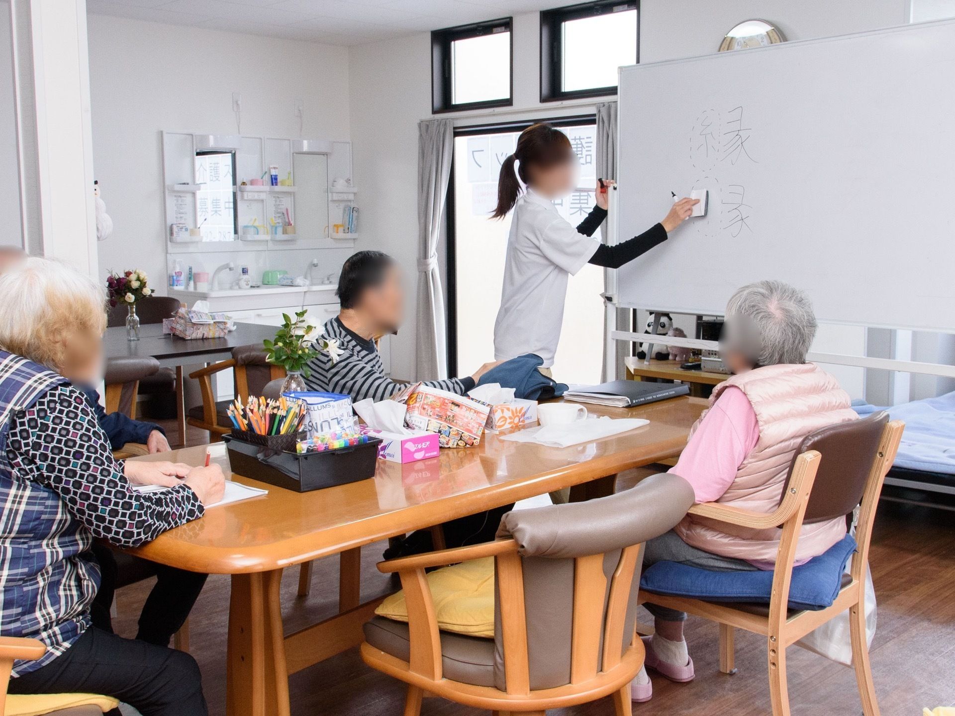 ３名の入居者様の前でホワイトボードで説明する女性スタッフ