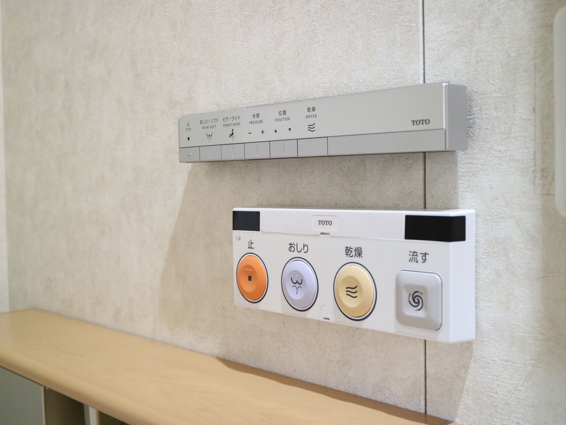 トイレに取り付けられた温水洗浄便座のパネルの画像である。２ヵ所に分かれており、ボタンの大きなものと小さなものがある。