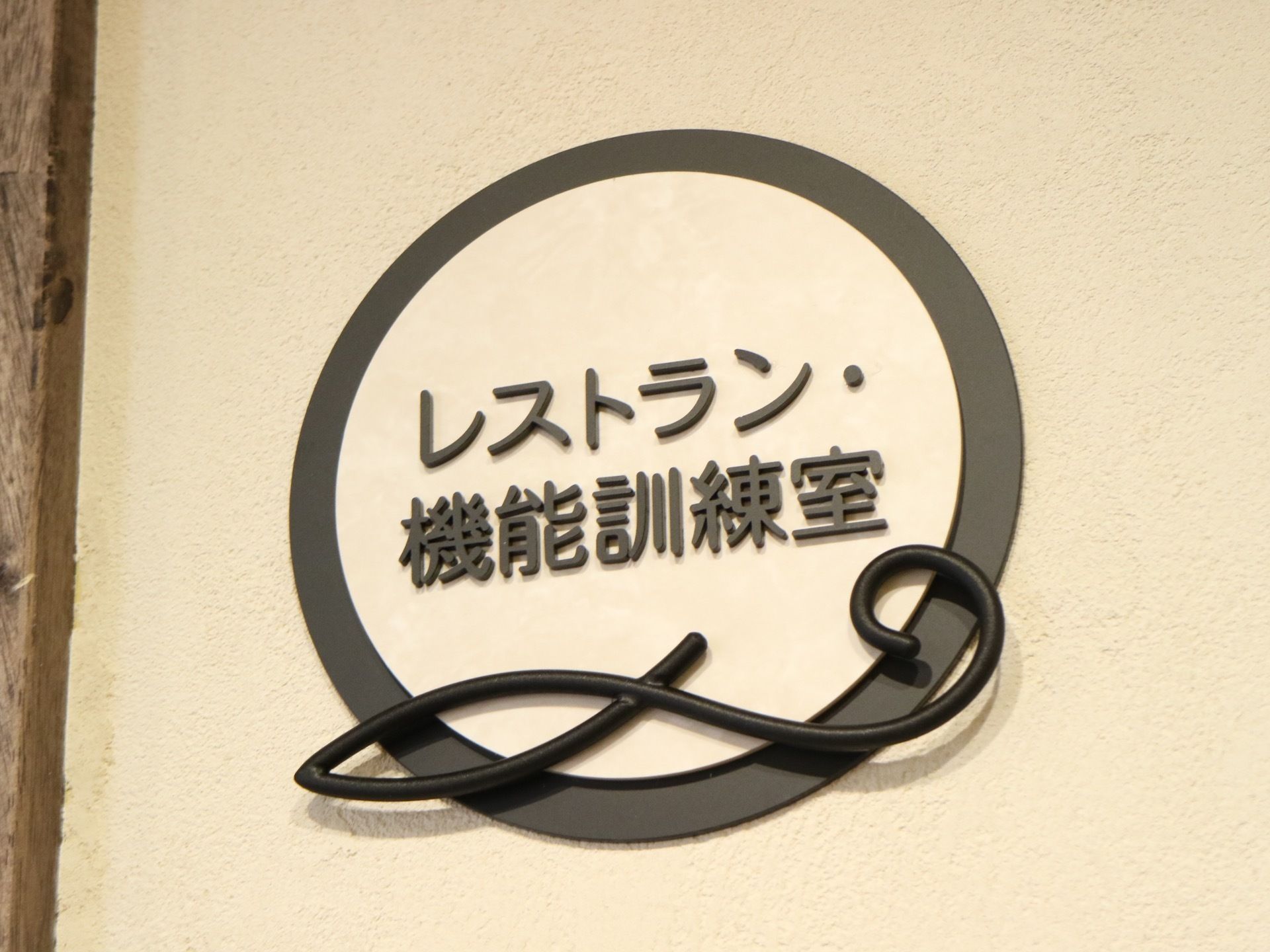 廊下の壁に取り付けられた部屋名のプレートで、レストランと機能訓練室の入口のものである。見やすいゴシック体で書かれている。