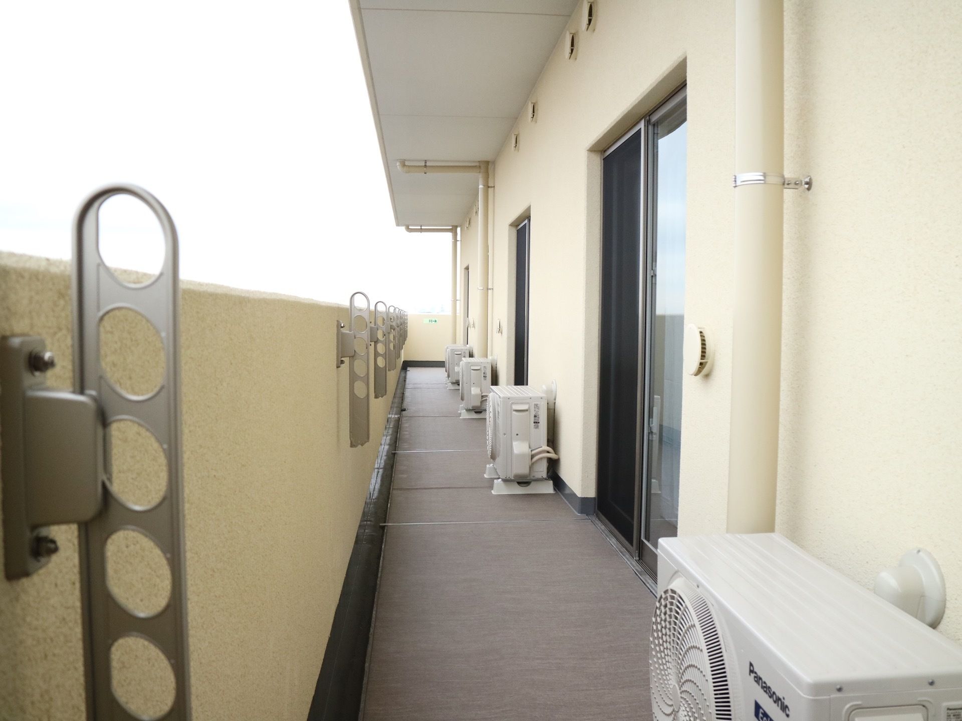 各部屋から出られるベランダはすべてつながっている。壁際に室外機が並べられている。外に面した柵の内側に物干し台がある。