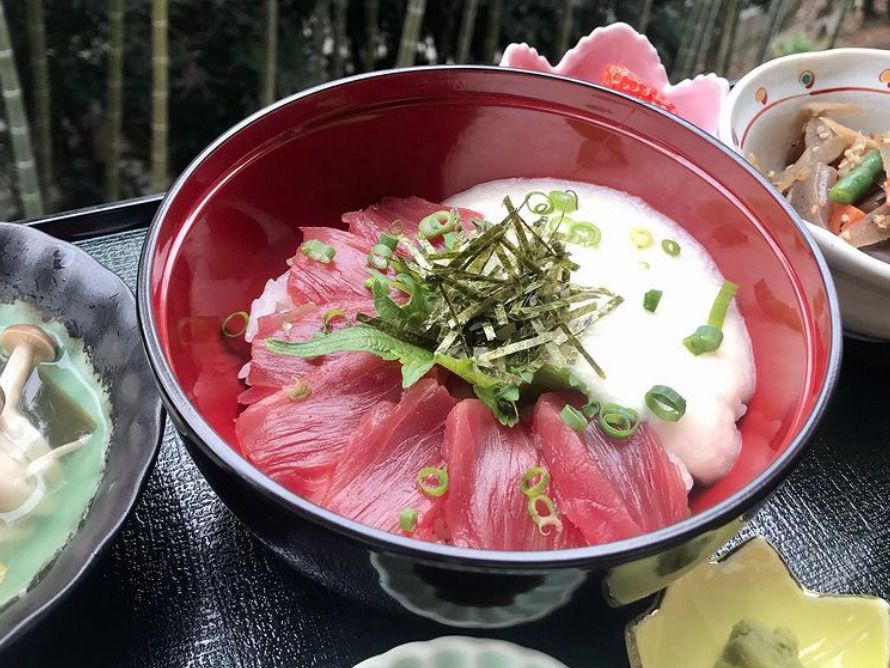 マグロととろろ芋の乗ったどんぶりと、野菜やきのこの料理が小鉢に盛り付けてある