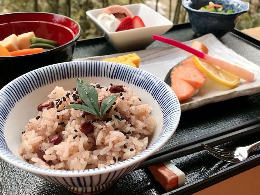 赤飯と焼き鮭、小鉢に盛られた野菜のおかずに箸とフォークが添えられている