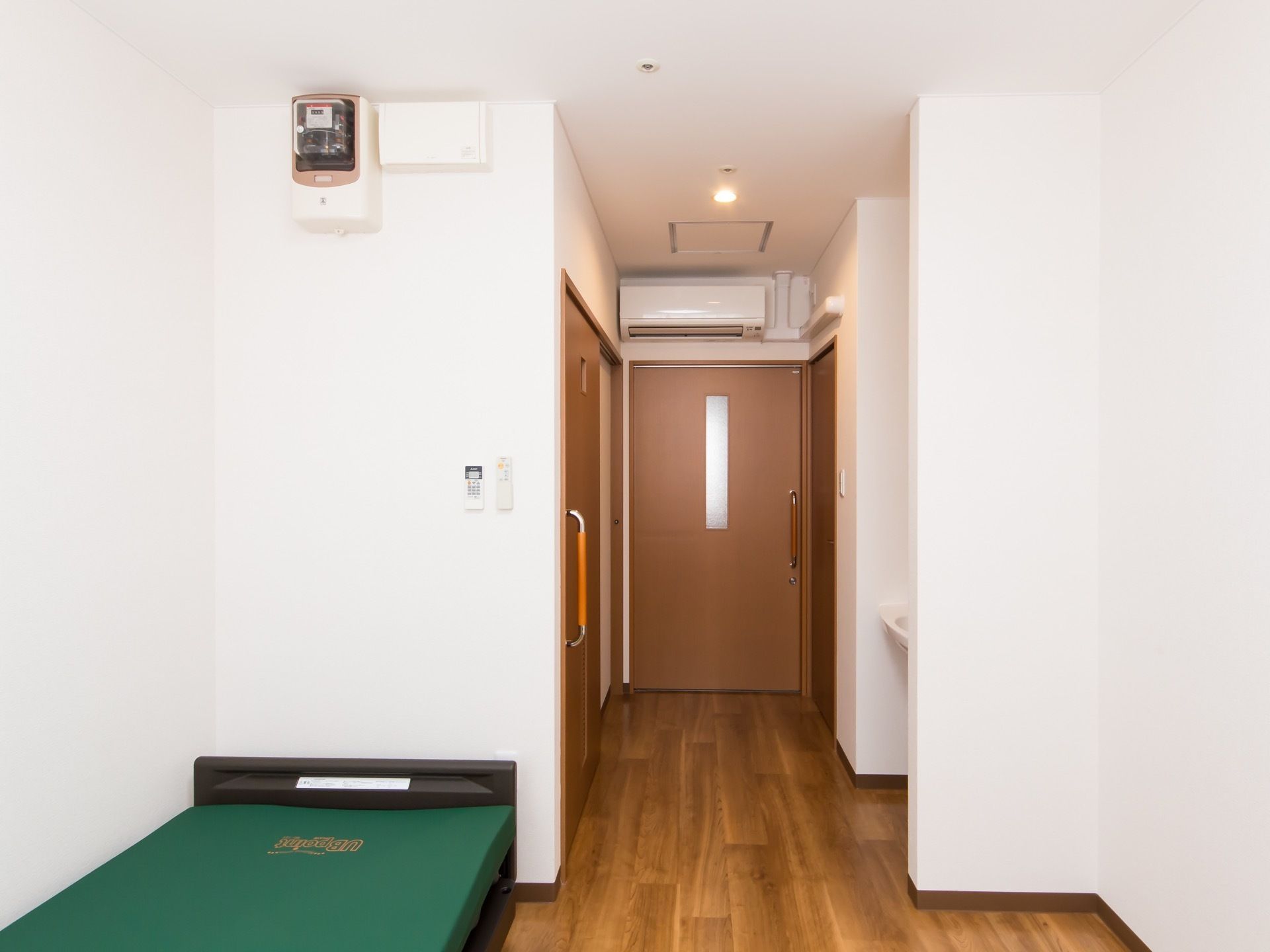 入口近くに、トイレやクローゼット、洗面台が備わった居室で、エアコンが設置されている。室内にベッドが置かれている。