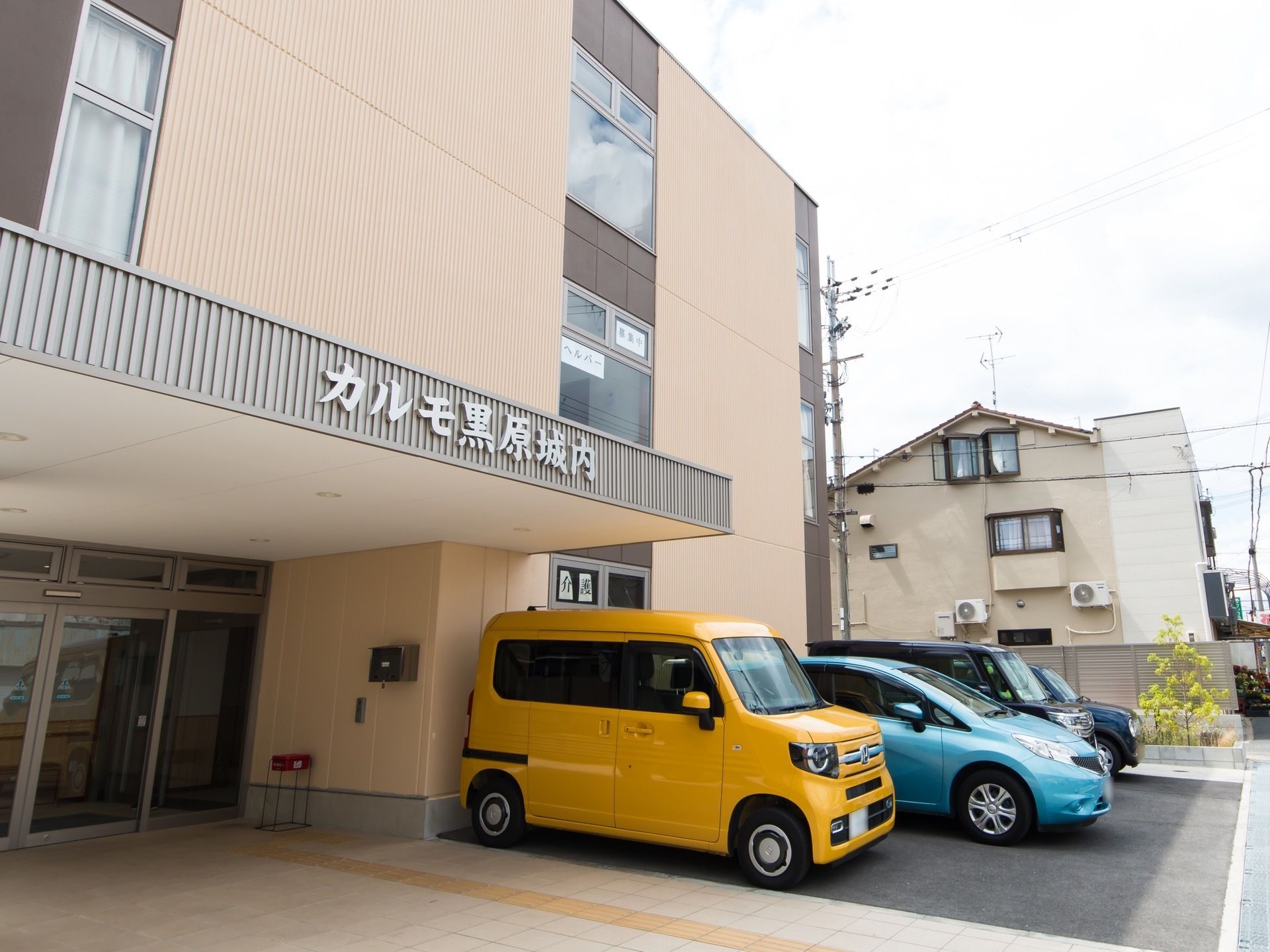 茶色とピンク色の外壁の３階建ての建物で、駐車スペースが備わっている。入口は自動ドアで、玄関前には広い屋根がある。