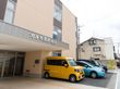 茶色とピンク色の外壁の３階建ての建物で、駐車スペースが備わっている。入口は自動ドアで、玄関前には広い屋根がある。