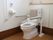 清潔感のある白い便座。トイレ室内は広く、車椅子や介助者も入れるスペースがある。立ち上がる際の手すりなどが設置されている。