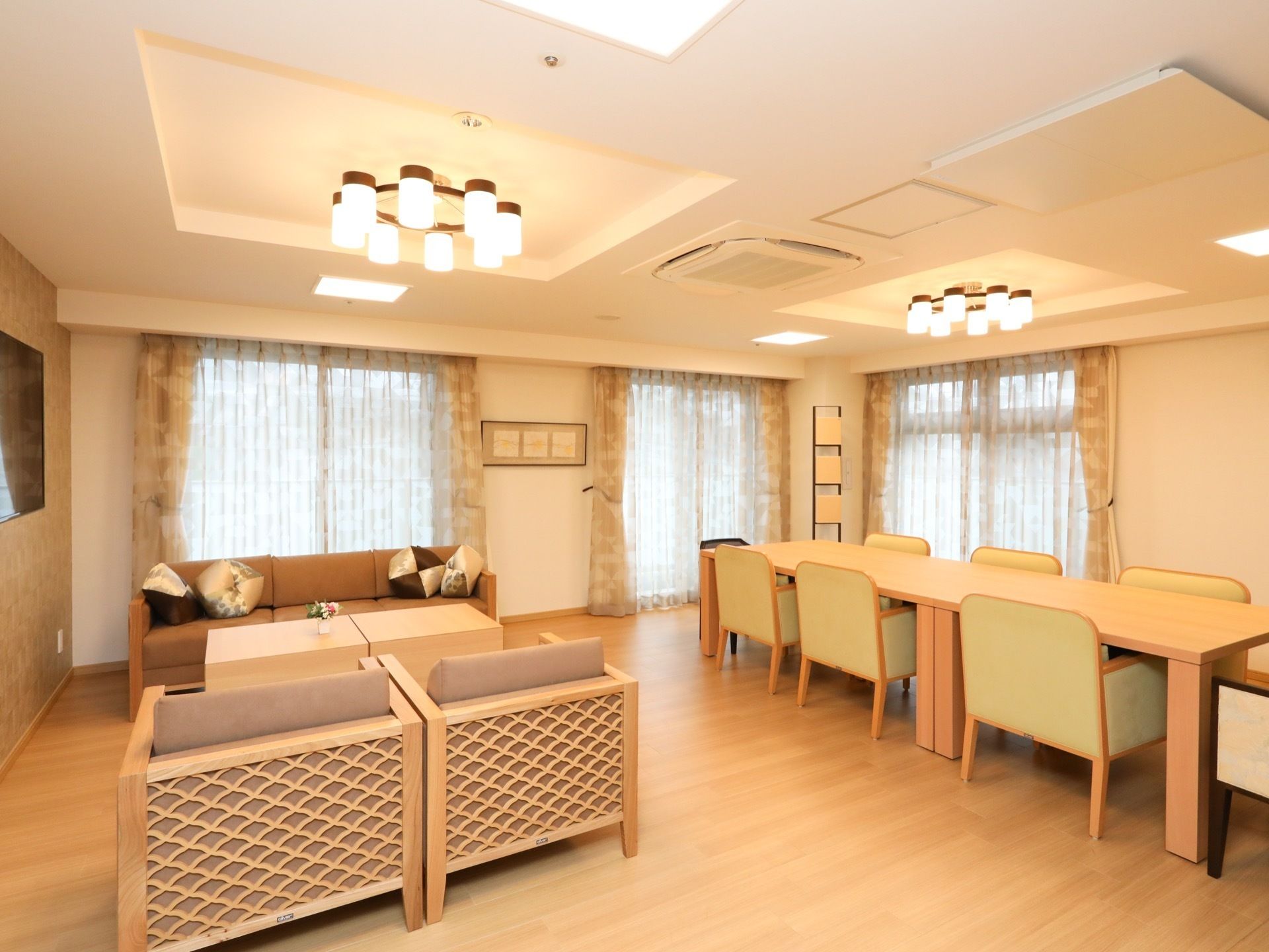 たくさんの椅子やテーブルが整然と置かれた広々とした部屋がある。天井にモダンな照明器具が２つ設置され、点灯している。