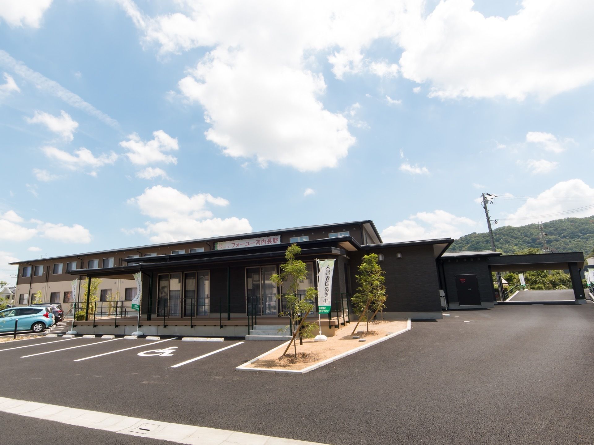 茶色とベージュ色の2階建の建物と、ダークグレーの平屋の建物が建っている。駐車場には車椅子をご利用の方優先のスペースがある。
