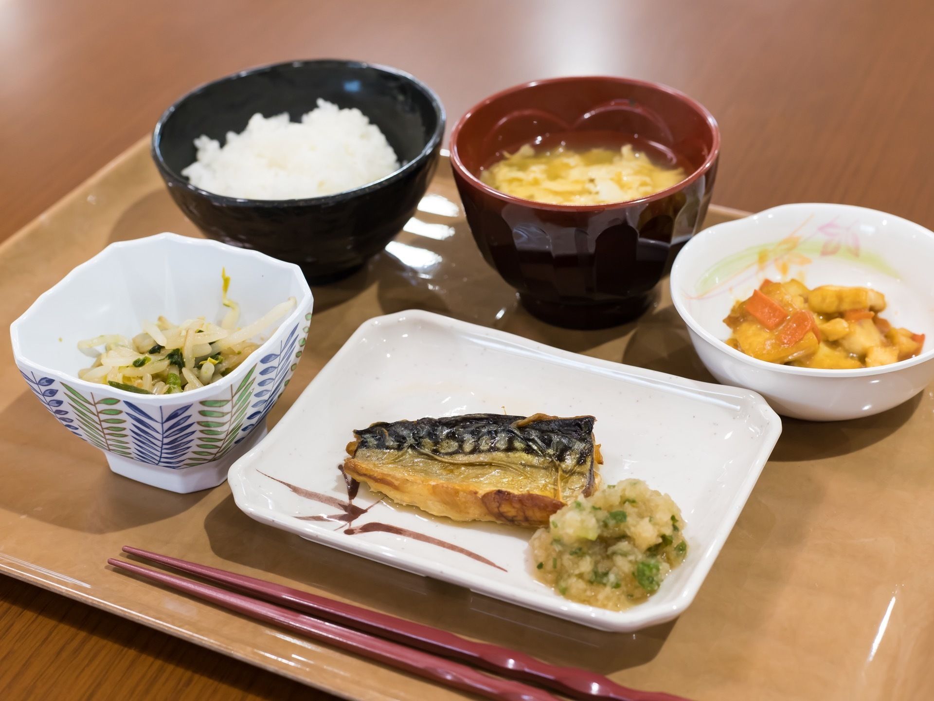 トレーに一名様分の食事を用意。メインディッシュは魚料理で、ご飯とみそ汁のほかに小鉢が二品ある。