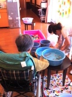 車いすの男性が見下ろす先に、金魚の泳ぐ桶がある。奥にはごく小さいプールがあり、中にヨーヨーが浮かんでいる。
