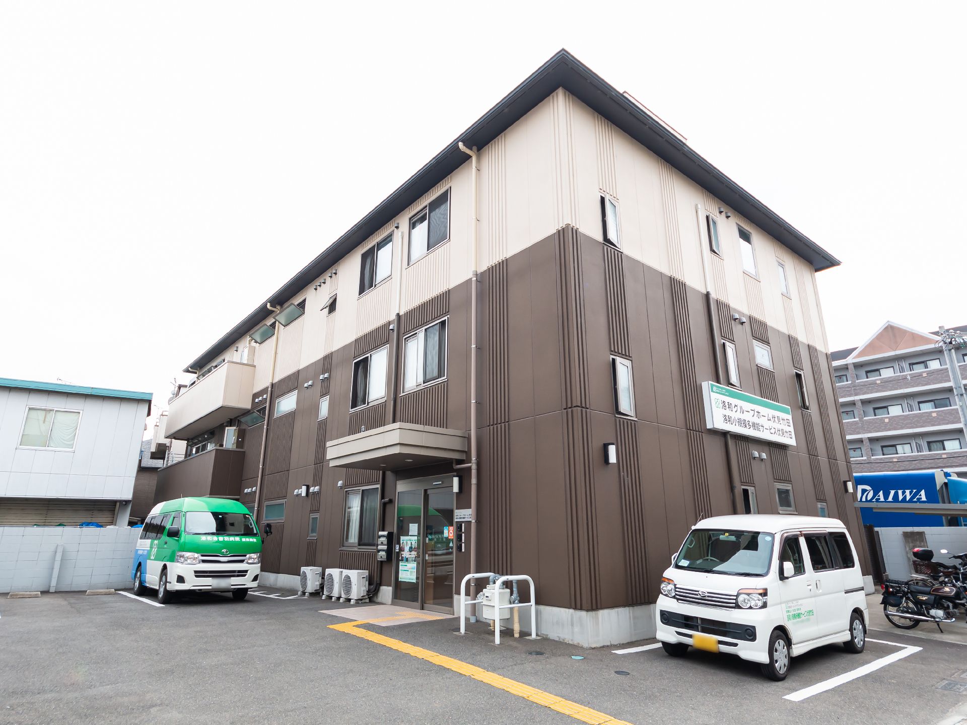 ブラウン系の3階建ての建物の1番上の階の外壁はベージュ。敷地内には駐車場が設置されている。