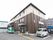 ブラウン系の3階建ての建物の1番上の階の外壁はベージュ。敷地内には駐車場が設置されている。