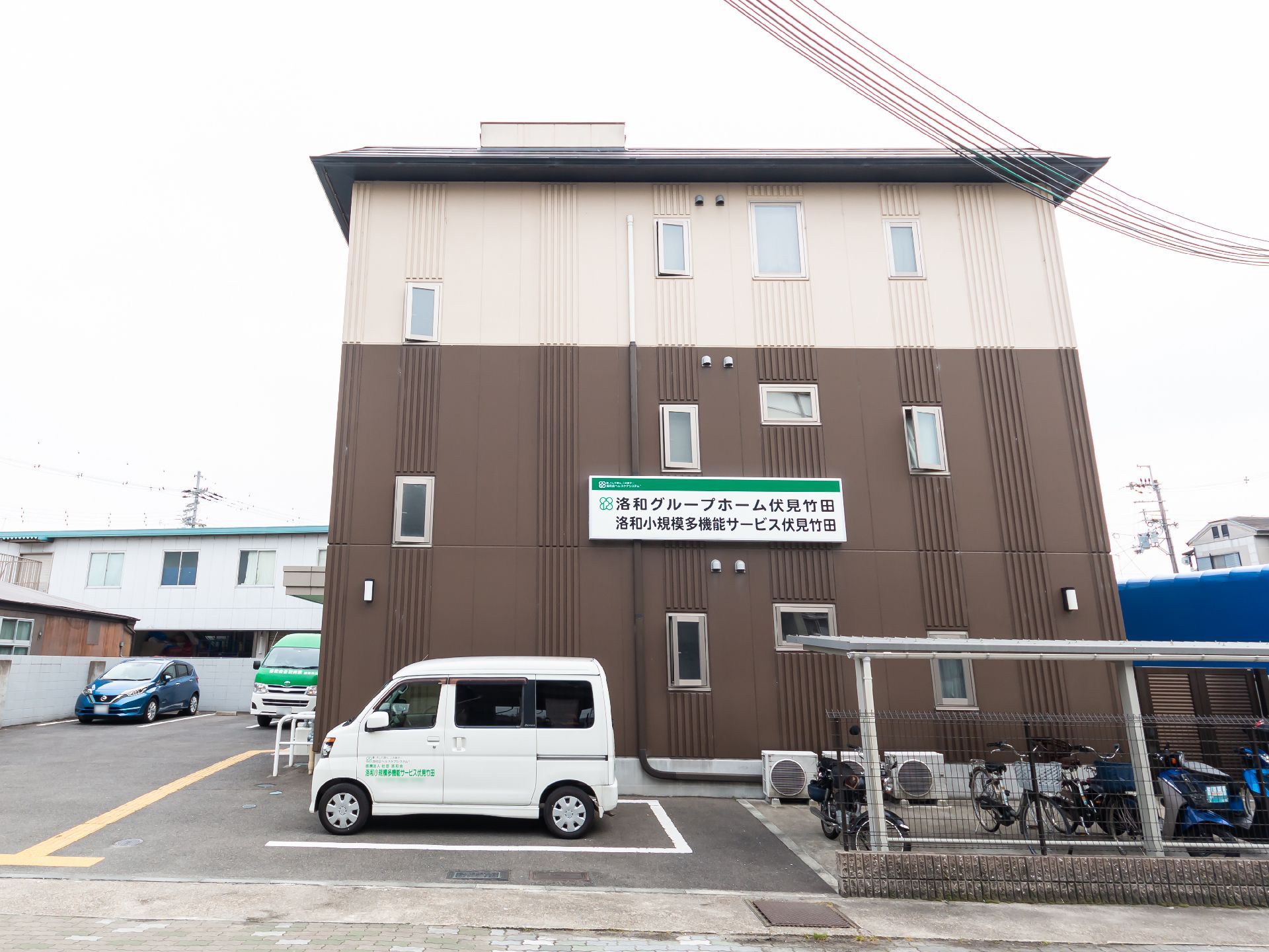 ブラウンとベージュの3階建ての建物の前には駐車スペースがある。
