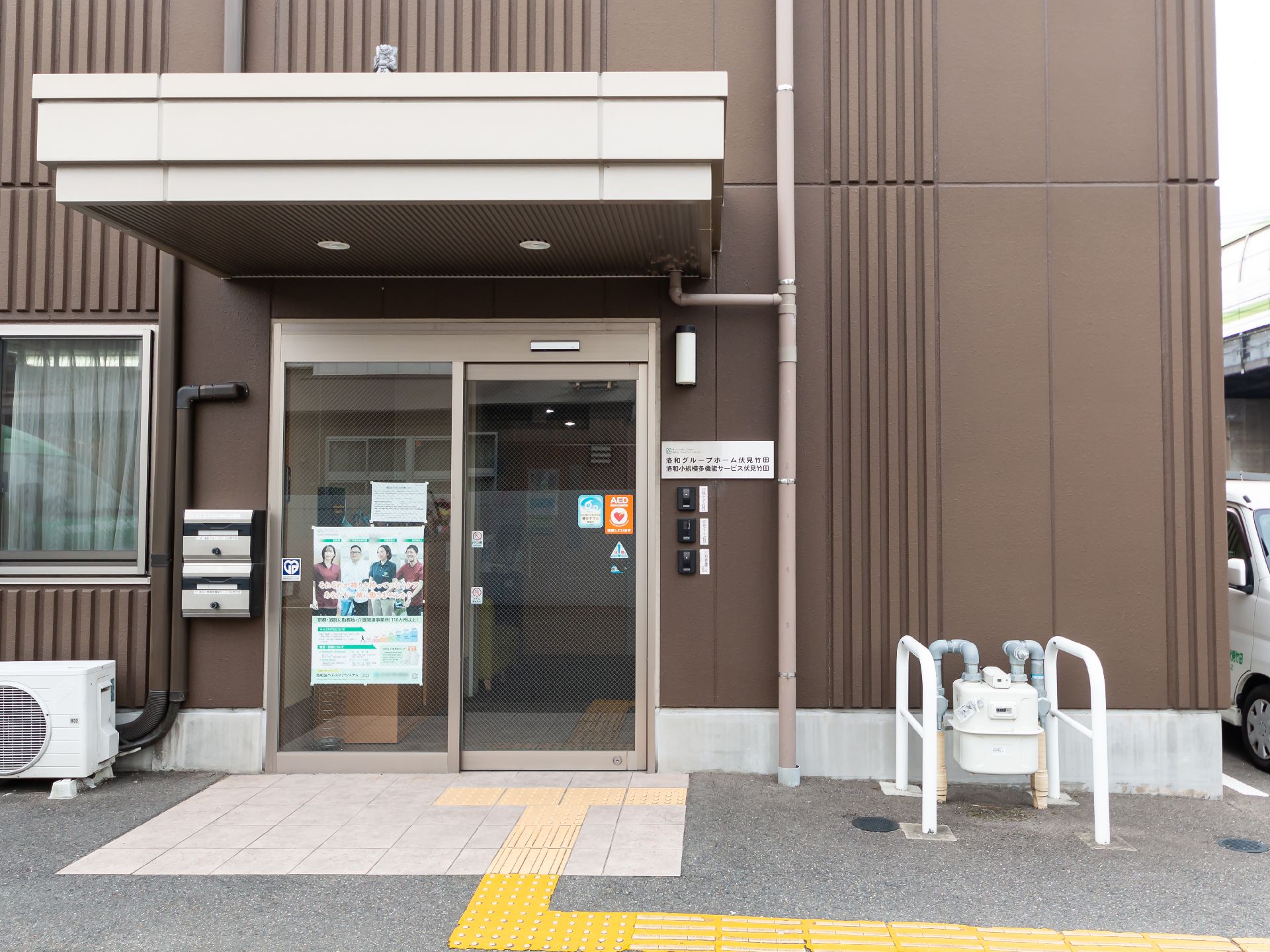 ベージュとブラウンの3階建ての建物の左側には駐車スペースがある。