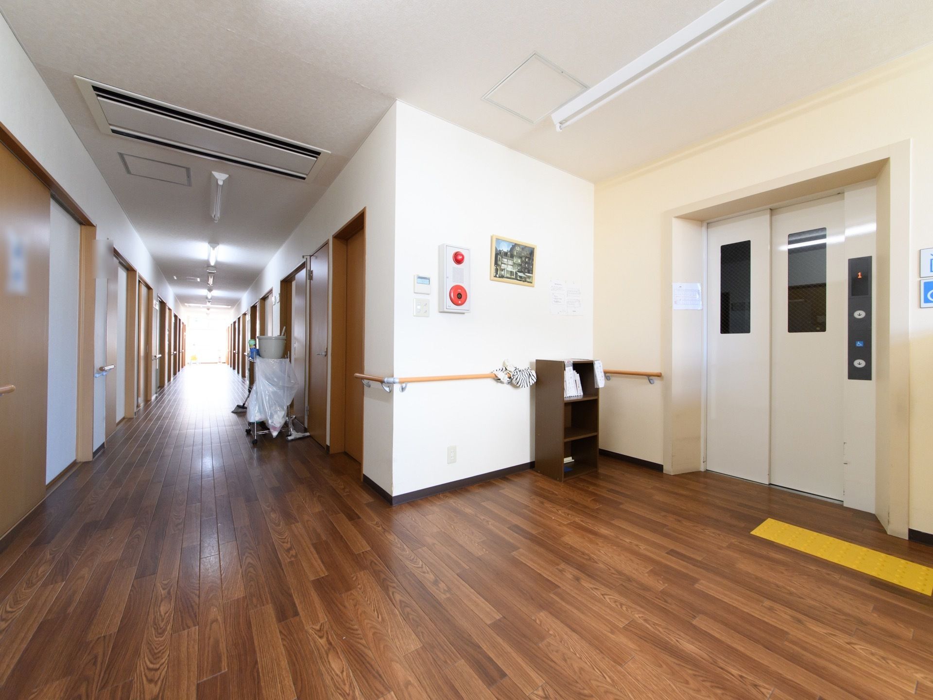 入居者様の居室の出入口がある共用廊下である。壁には転倒の防止のために、木製の手すりが設置されている。