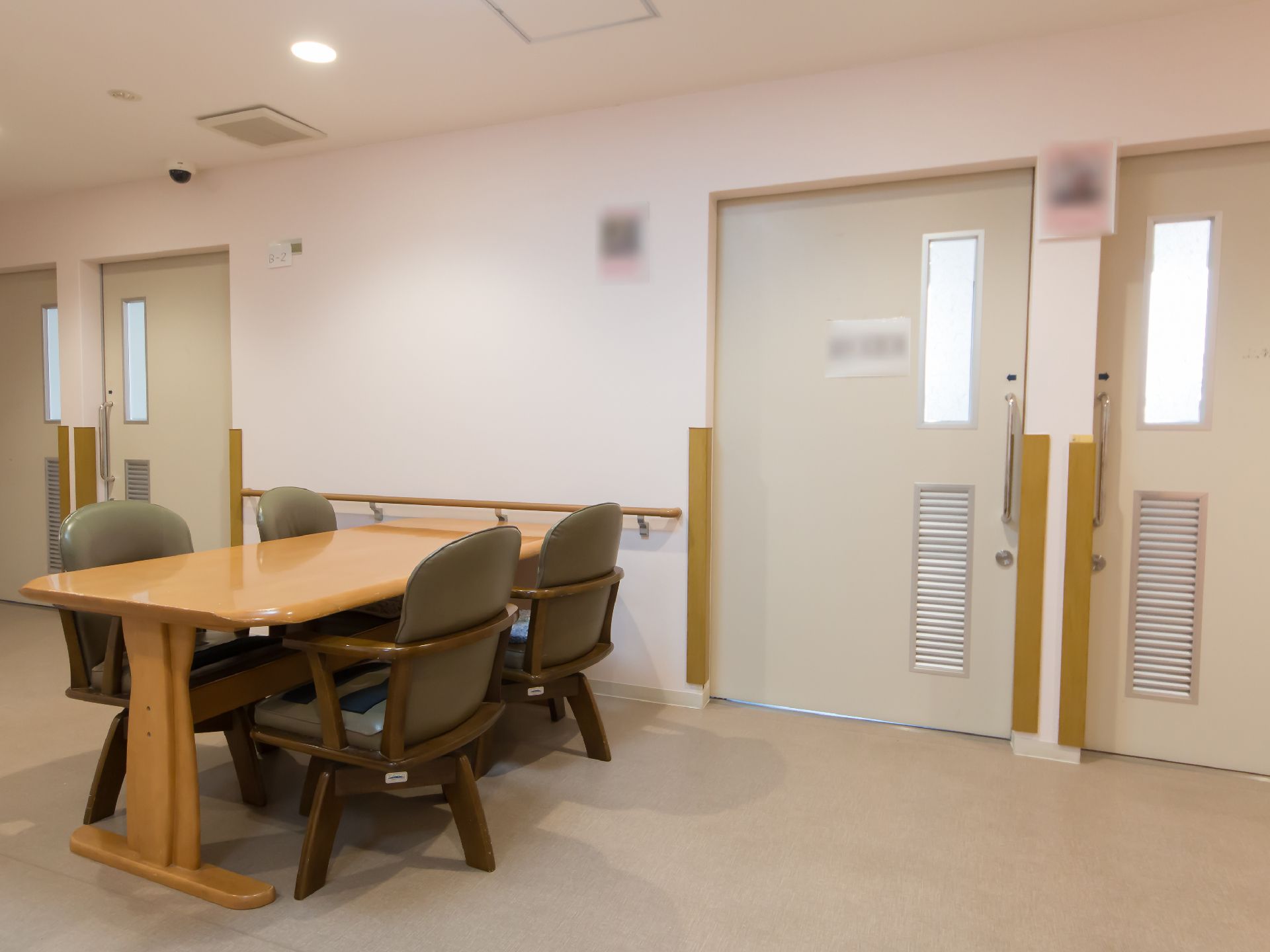 白色の壁沿いに木製のテーブルと椅子がある。各部屋のドアが複数あり、そばには手すりが設置されている。