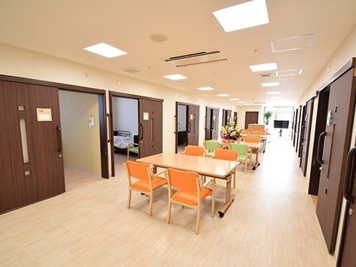 居室が両サイドにある幅の広い廊下にダイニングテーブルが複数置かれている。