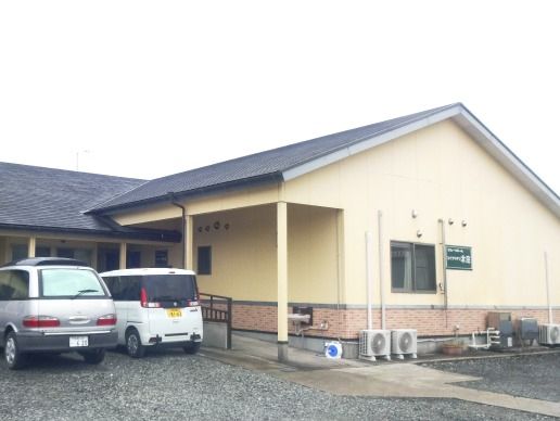 平屋建ての一軒家のような建物。手前に駐車場スペースがあり、入り口にスロープが付いている様子