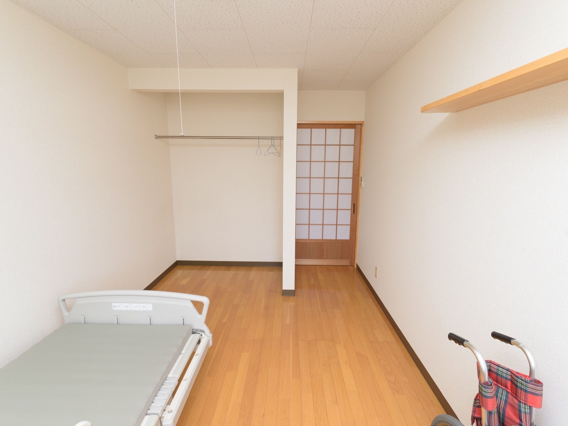 和洋折衷のデザインの居室。扉は障子風のデザインの引き戸、床はフローリングとなっている。ベッドと収納用のスペース、棚が備え付けられている。