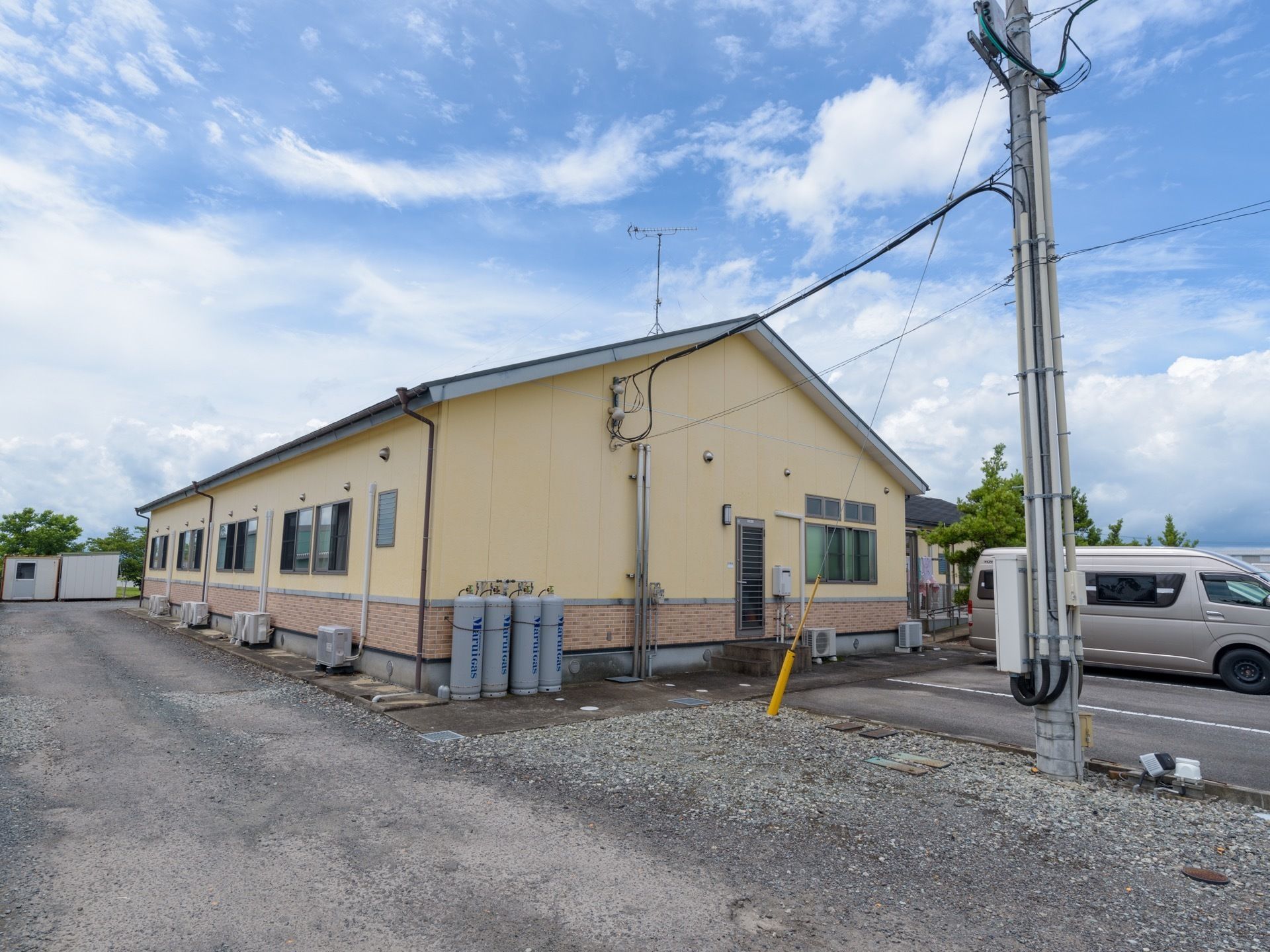 淡い黄色の壁の平屋建てのホーム。ホームの建物の横には駐車場もあり、自動車が駐車されているのが見える。