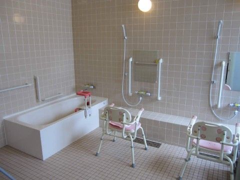 タイル張りの浴室。壁にある小さめの鏡の両横には手すりが付けられており、鏡の前にはイスが置かれている。