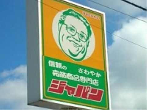 スーパーマーケットの巨大な看板。上半分がオレンジ、下半分が緑で、メガネをかけた男性の顔が上部の中央に描かれている。